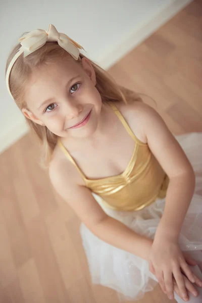 Pretty diligent ballet girl sitting in white tutu at dance studi