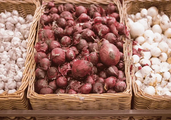 Bunch of red onion, white onion and garlic in wicker tray in supermarket