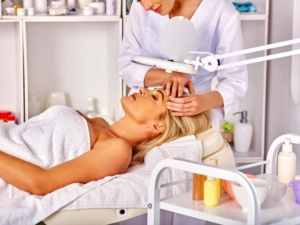 Woman middle-aged in spa salon. Tweezing eyebrow by beautician.