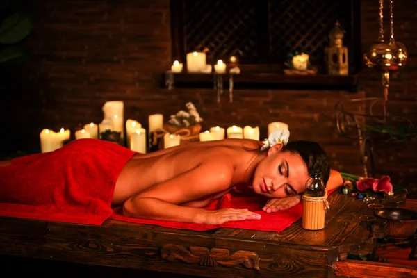Young woman lying on wooden spa bed in massage spa salon.