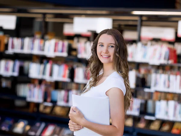 Happy female student holding books at the library