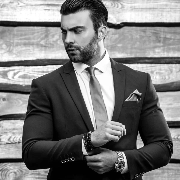 Black-white portrait of beautiful fashionable man in stylish suit against wooden background.