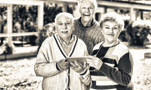 Three elder people using tablet outdoor