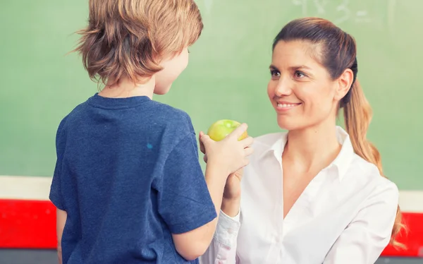 Female teacher with schoolboy handing apple