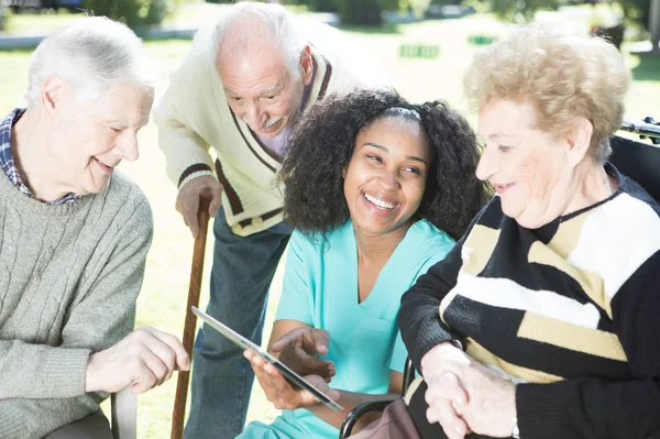 Three senior citizens in hospital garden learning to use tablet