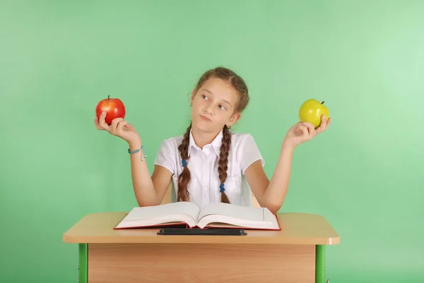 Girl in a school uniform sitting at the desk and eat apples