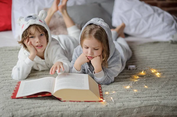 Two children lie on the big bed and read Christmas tales