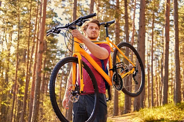 Man holds mountain bicycle on a shoulder.