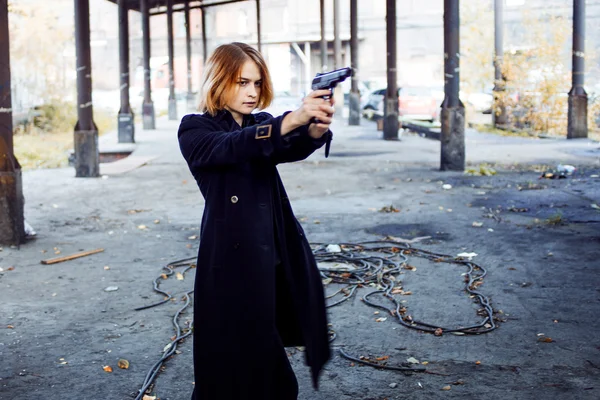 Woman pointing a gun. Mafia girl shooting at someone on the street.