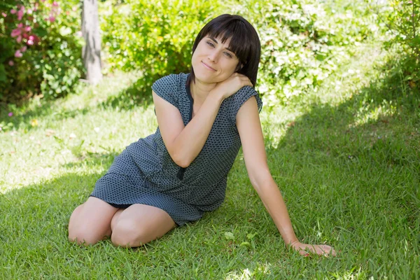 Casual woman posing seated, smiling at the camera, outdoors