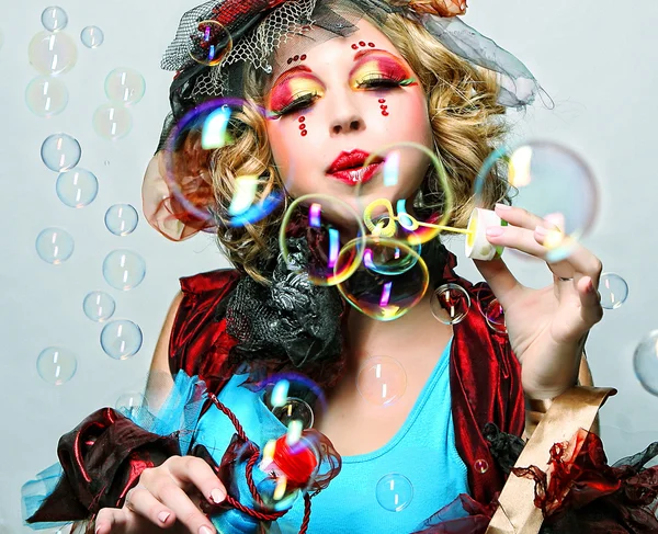 Fashion model with creative make-up blowing soap bubbles.