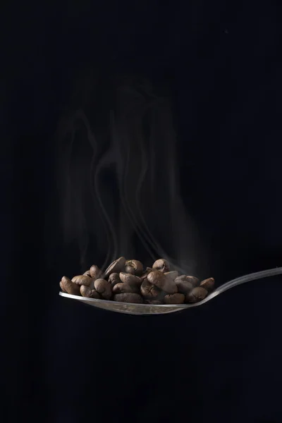 Silver spoon with coffee beans and steam on black