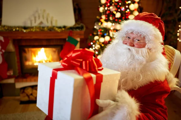 Santa Claus sitting by the fireplace with big present