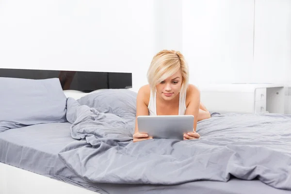 Beautiful woman lying on bed using digital tablet