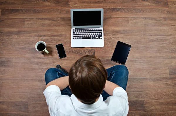 Young Adult Male Sitting on the Floor Thinking, Mobile Computing Devices and a Cup of Coffee in Front of Him - Study or Freelance Work Concept