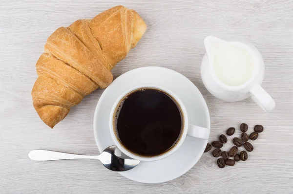 Coffee, croissant, milk jug and coffee beans on table