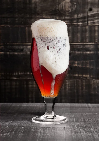 Glass of brown ale beer with foam on wood