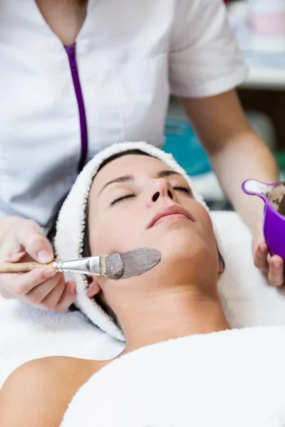 Beautiful young woman with clay facial mask in beauty spa. Detox