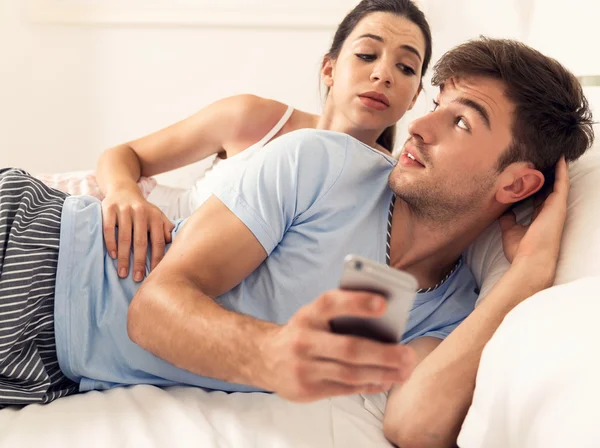 Man on bed texting while woman looking