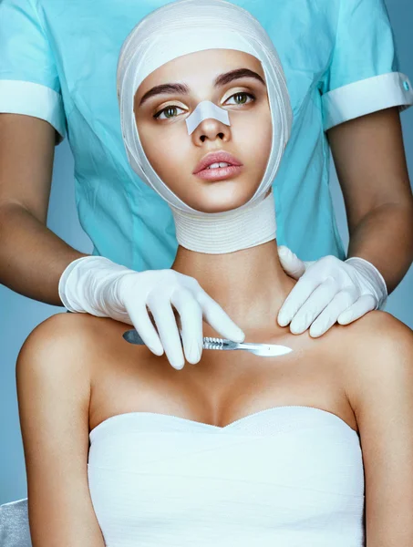 Beautiful woman wrapped in medical bandages and plastic surgeon holding scalpel near her breast.