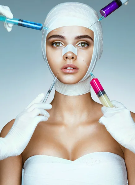 Pretty woman in medical bandages and beauticians hands with syringes making botox injection in her face