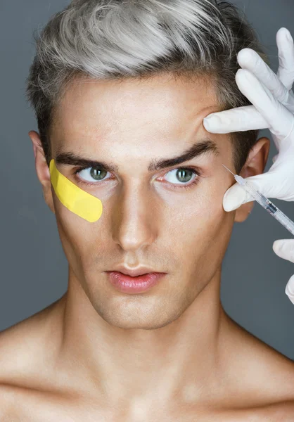 Glamorous man gets beauty injection in eye area from doctor.
