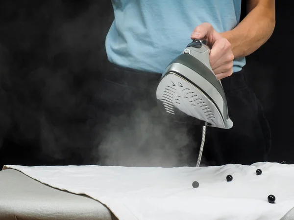 Male person using a steaming hot iron, on a white shirt