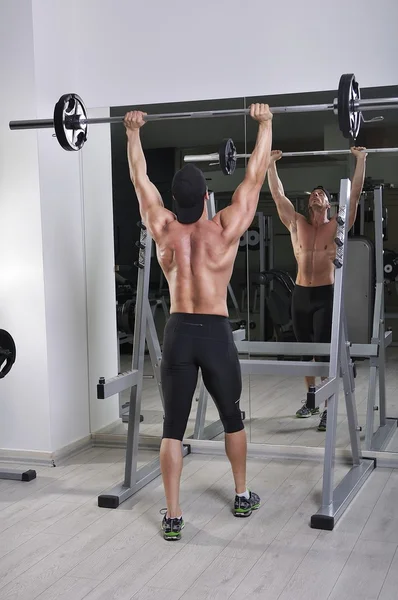 Handsome powerful athletic man doing barbell shoulder press exercise. Strong bodybuilder with perfect muscles.