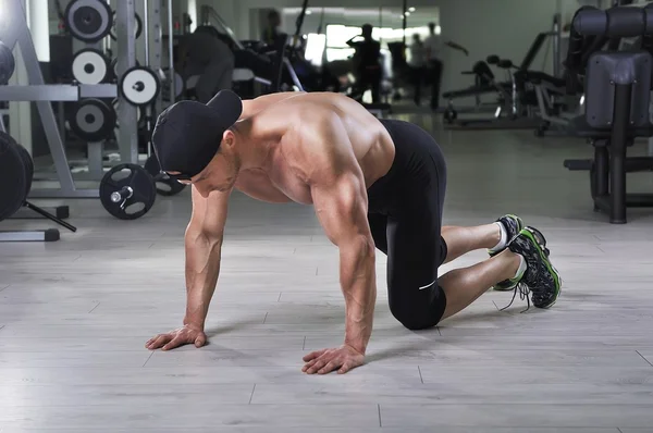 Handsome powerful athletic man preparing for performing push ups at the gym. Strong bodybuilder with perfect back, shoulders, biceps, triceps and chest.