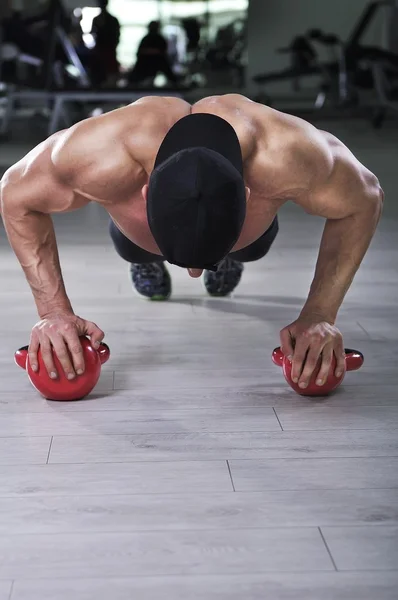 Handsome powerful athletic man performing push ups with kettle bell. Strong bodybuilder with perfect shoulders, biceps and triceps.