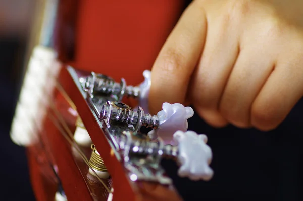 Closeup neck of beautiful acoustic guitar being tuned by woman sitting down, musician concept