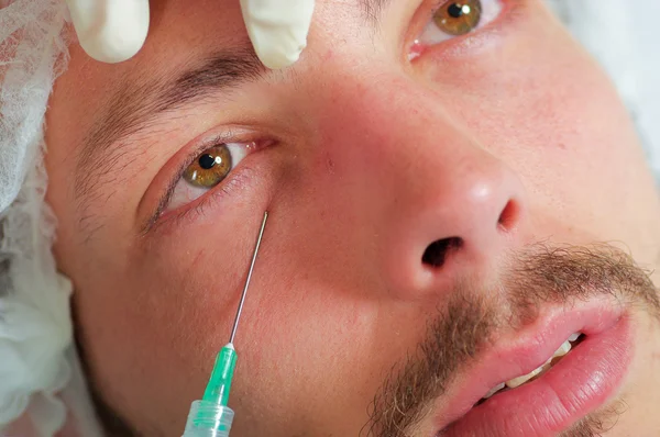 Closeup young mans face receiving facial cosmetic treatment injections, doctors hand with glove holding syringe