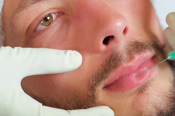 Closeup young mans face receiving facial cosmetic treatment injections, doctors hand with glove holding syringe