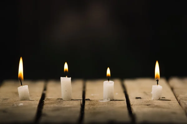 Four white wax candles sitting on wooden surface burning with black background, beautiful light setting