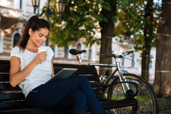 Woman with cup of coffee and using tablet outdoors