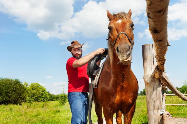 Cowboy saddling brown horse