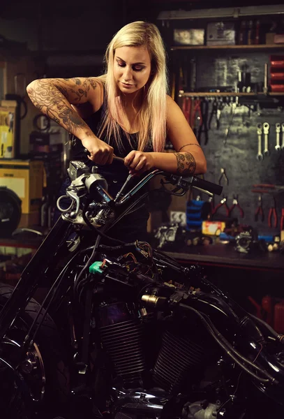 Blond woman mechanic repairing a motorcycle in a workshop