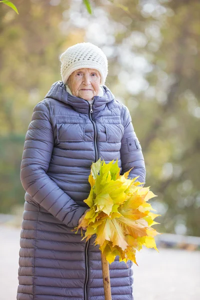 Senior woman with bunch of autumn leaves walking in park