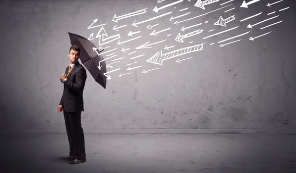 Business man standing with umbrella and drawn arrows hitting him