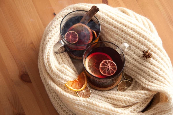 Seasonal and holidays concept Christmas mulled wine with beautiful orange slices inside the glass and some smoke , covered with warm white scarf . Very warm and cozy atmosphere Close up