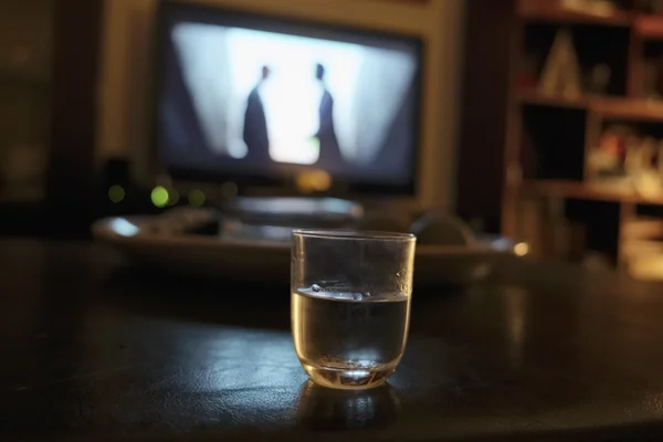 A glass of alcoholic drink in front of the TV at night in a living room