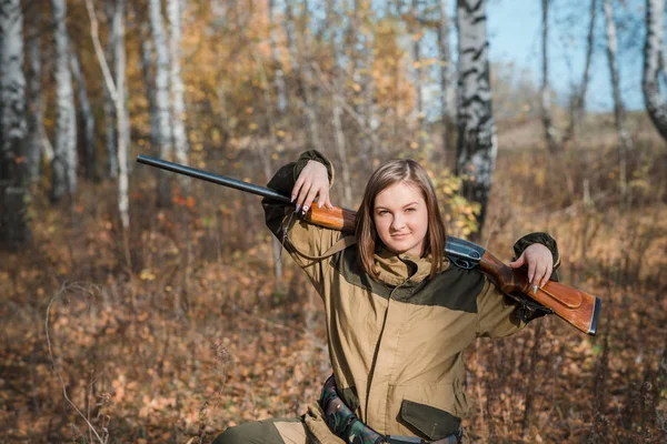 Portrait of a beautiful young girl hunter in camouflage clothes in the deciduous forest in nature with a gun