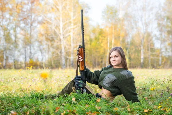 Portrait of a beautiful young girl hunter in camouflage clothes in the deciduous forest in nature with a gun