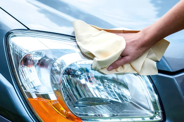 Hands of a beautiful young girl washing a car with a cloth microfiber wipes headlights and inner panel of the car, hand car wash