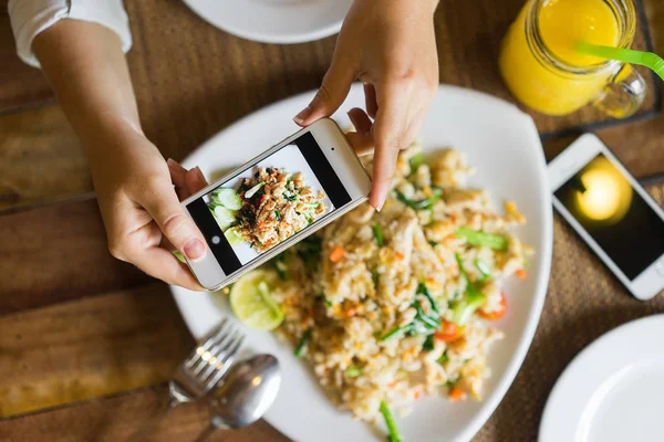 Hands with the phone close-up pictures of food. Fried rice with chicken and mango shake, one dish for two.