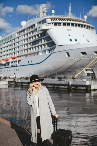 Beautiful woman traveler with suitcase talking on the phone in the sea cruise liner