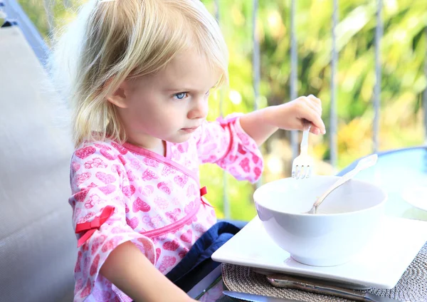 Little girl in adorable pink dress eating outside at summertime