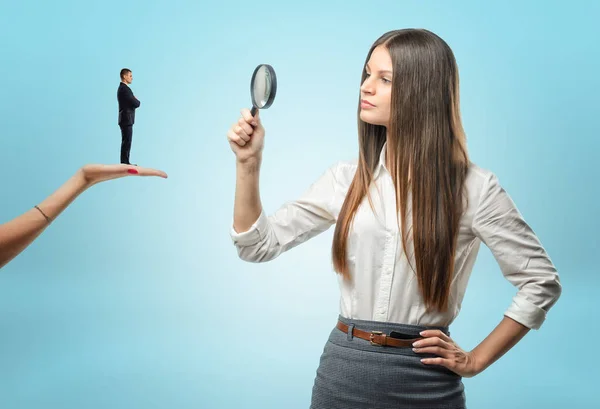 Young woman looking at tiny man with magnifying glass