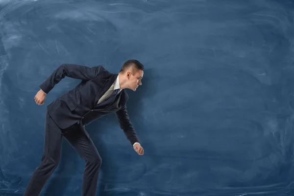Businessman standing as if he is going to run or pursue his goal on the blue chalkboard background.