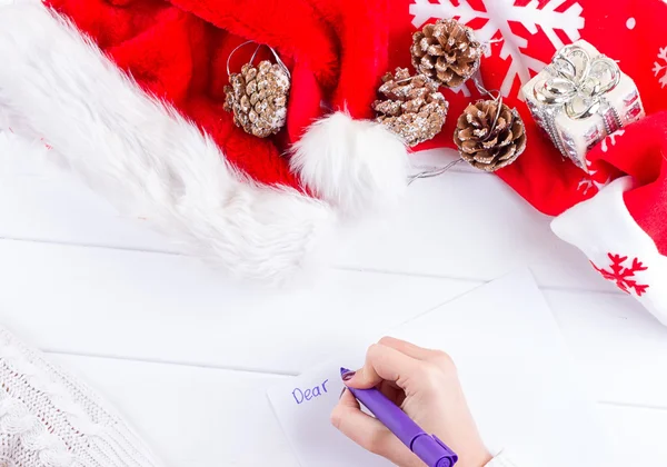 Female writing wish list in notebook near christmas gifts